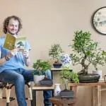 persoon met bonsai boekje en meerdere bonsai